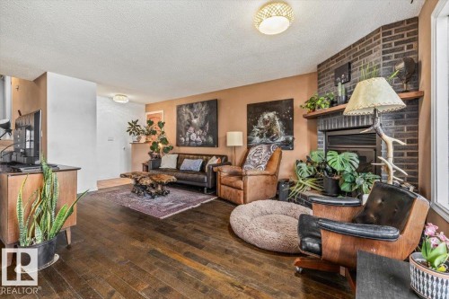 Living area featuring wood-finish flooring, a corner brick fireplace with mantel, and a large window - 135 Homestead Crescent Nw, Edmonton, AB 