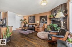 Living area featuring wood-finish flooring, a corner brick fireplace with mantel, and a large window - 