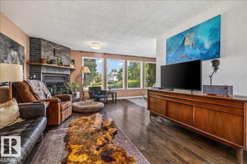 Spacious living area featuring wood-finish flooring, a corner fireplace with a dark brick surround and wood mantel, and expansive windows - 135 Homestead Crescent Nw, Edmonton, AB 