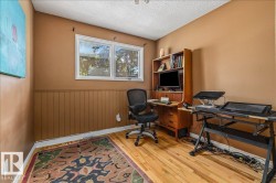 Room featuring wood-finish flooring, two large windows, a built-in wood-tone desk with shelving, and vertical wood paneling - 