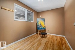 Wood-finish flooring with white baseboards, a single window with white trim, and a wall-mounted wooden coat rack - 