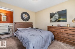 Bedroom featuring wood-finish headboard, textured carpeting, and direct access to a private bathroom - 