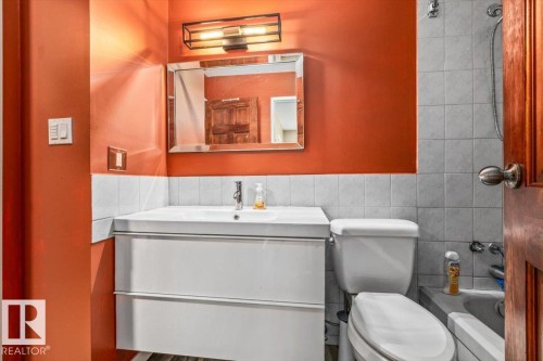 Bathroom featuring an orange accent wall, white vanity with integrated sink, rectangular wall mirror, and a modern light fixture - 135 Homestead Crescent Nw, Edmonton, AB 