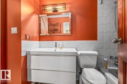 Bathroom featuring an orange accent wall, white vanity with integrated sink, rectangular wall mirror, and a modern light fixture - 