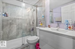 Contemporary bathroom featuring a glass-enclosed shower with gray patterned tile, a built-in shower niche, and a white vanity with integrated sink and chrome faucet - 