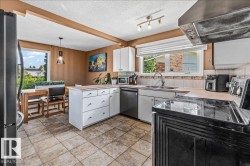 Kitchen featuring neutral-toned tile flooring, white cabinetry, a built-in dishwasher, a stainless steel sink, and a range hood - 
