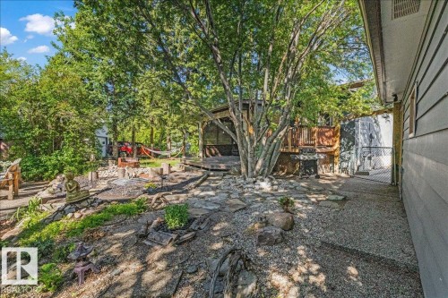 Extensive backyard featuring a flagstone patio, gravel pathways, and a raised wood deck with screened enclosure - 135 Homestead Crescent Nw, Edmonton, AB 