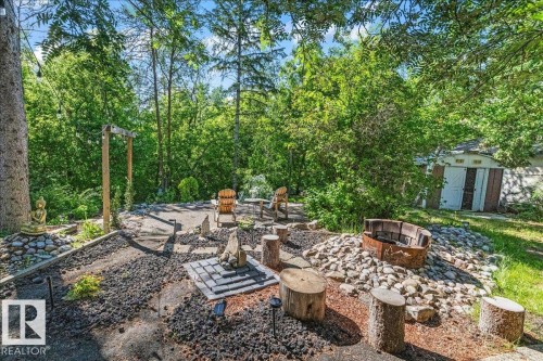 Expansive outdoor retreat featuring a fire pit area with stone and wood seating, a paved patio, and mature trees providing natural screening - 135 Homestead Crescent Nw, Edmonton, AB 