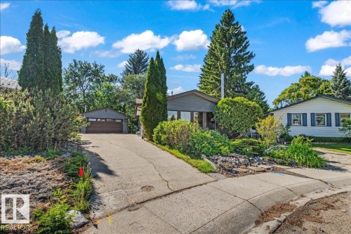 Mature landscaping frames the property, featuring a concrete driveway leading to a detached garage - 135 Homestead Crescent Nw, Edmonton, AB 