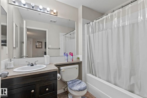 Bathroom featuring a dark wood-finish vanity with an integrated sink, a large wall-mounted mirror, a tub/shower combination with white tile surround, and neutral-toned flooring - 2106 9357 Simpson Dr Nw, Edmonton, AB - Indoor Photo Showing Bathroom