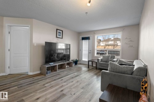 Spacious living area featuring light-toned walls, wood-finish flooring, and ample natural light from a large window - 2106 9357 Simpson Dr Nw, Edmonton, AB - Indoor Photo Showing Living Room