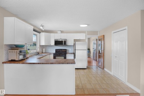 Well-appointed kitchen featuring white cabinetry, a mosaic tile backsplash, a built-in microwave, and a breakfast bar - 13524 26 Street, Edmonton, AB 