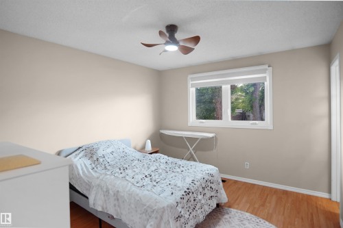 Room featuring wood-finish flooring, a ceiling fan with integrated lighting, and a window with roller shades - 13524 26 Street, Edmonton, AB 