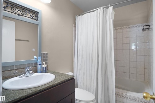 Bathroom featuring a vanity with an undermount sink, a dark wood-finish cabinet, and a speckled countertop - 13524 26 Street, Edmonton, AB 