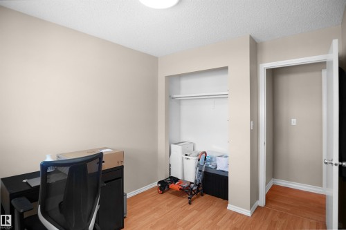 Neutral-toned room featuring wood-finish flooring, a built-in closet with shelving and hanging rod, and a doorway with white trim - 13524 26 Street, Edmonton, AB 