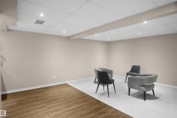 Spacious room featuring neutral painted walls, dual flooring materials including wood-finish planks and light-toned tiling, a drop ceiling with recessed lighting, and crisp white baseboards - 