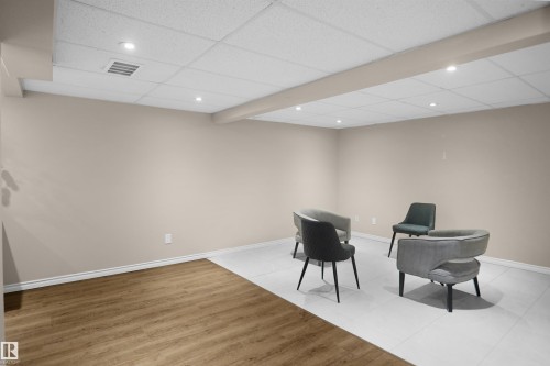 Spacious room featuring neutral painted walls, dual flooring materials including wood-finish planks and light-toned tiling, a drop ceiling with recessed lighting, and crisp white baseboards - 13524 26 Street, Edmonton, AB 
