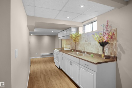 Kitchenette featuring white cabinetry, a double basin stainless steel sink, and a speckled countertop - 13524 26 Street, Edmonton, AB 