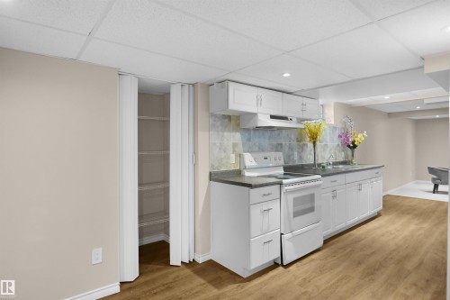 Kitchenette featuring white cabinetry, a built-in range, and a stainless steel sink with a tiled backsplash - 13524 26 Street, Edmonton, AB 
