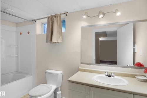 Bathroom featuring a tub/shower combination, window with privacy curtain, and a vanity with an integrated sink and track lighting fixture - 13524 26 Street, Edmonton, AB 
