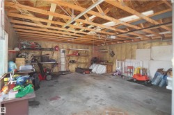 Spacious garage featuring exposed wood beam ceiling, concrete flooring, window for natural light, wall-mounted shelving, and insulated walls - 