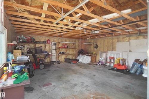 Spacious garage featuring exposed wood beam ceiling, concrete flooring, window for natural light, wall-mounted shelving, and insulated walls - 13524 26 Street, Edmonton, AB 