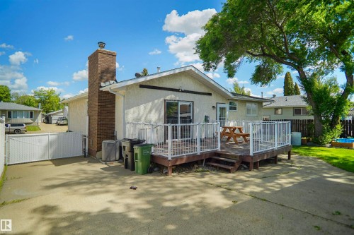 Rear exterior featuring a wood-decked patio with white railings, a prominent brick chimney, and a concrete driveway - 13524 26 Street, Edmonton, AB 