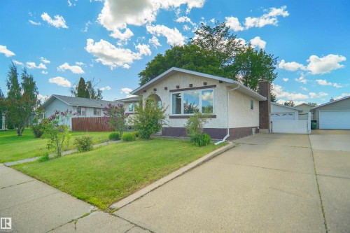 Stucco exterior featuring an arched window, a concrete driveway, and a front lawn with mature landscaping - 13524 26 Street, Edmonton, AB 
