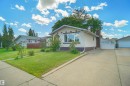 Stucco exterior featuring an arched window, a concrete driveway, and a front lawn with mature landscaping - 13524 26 Street, Edmonton, AB 