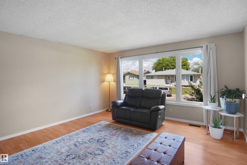 Spacious living area featuring large picture windows, wood-finish flooring, light neutral wall tones, and white baseboards - 13524 26 Street, Edmonton, AB 