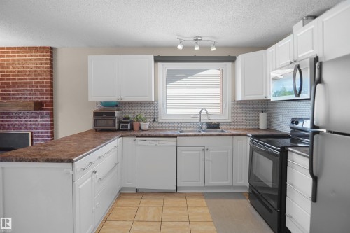 Kitchen featuring white cabinetry, brown countertops, tile flooring, and a subway tile backsplash - 13524 26 Street, Edmonton, AB 