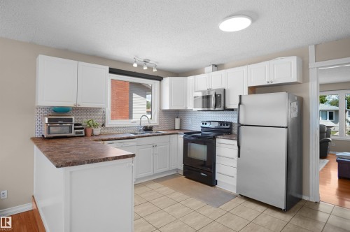 Kitchen featuring white cabinetry, a U-shaped countertop configuration, stainless steel appliances, a tile backsplash, and tile flooring - 13524 26 Street, Edmonton, AB 
