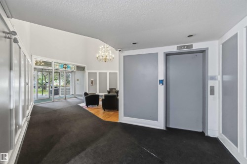 Lobby area featuring dual glass entry doors with a decorative transom, a prominent chandelier, recessed lighting, and a passenger elevator - 121 5125 Riverbend Road Nw, Edmonton, AB 