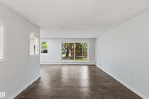 Spacious room featuring wood-finish flooring, light grey walls, and a large sliding glass door - 121 5125 Riverbend Road Nw, Edmonton, AB 
