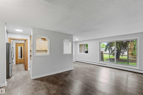 Spacious room featuring wood-finish flooring, light grey wall paint, and white baseboards - 121 5125 Riverbend Road Nw, Edmonton, AB 