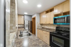 Modern kitchen featuring light wood cabinetry, a double basin stainless steel sink, a stainless steel French door refrigerator, and a black electric range - 