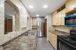 Kitchen featuring light wood cabinetry, stone-finish countertops, and a full tile backsplash - 