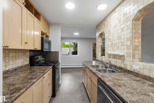 Kitchen with light wood-finish cabinetry, dark speckled countertops, and a full tile backsplash - 121 5125 Riverbend Road Nw, Edmonton, AB 