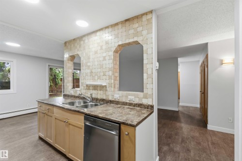 Kitchen island featuring a double-basin stainless steel sink, wood-finish cabinetry, and a stainless steel dishwasher - 121 5125 Riverbend Road Nw, Edmonton, AB 