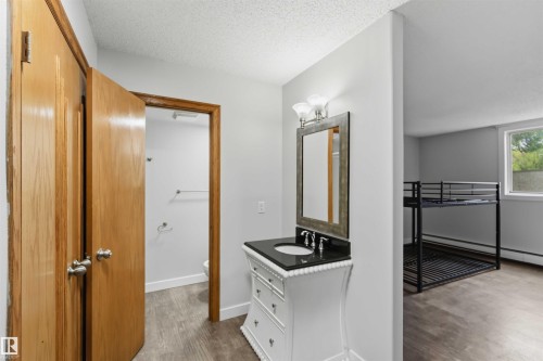 Bathroom vanity with a dark countertop and undermount sink, framed by a wall-mounted mirror and tri-light fixture - 121 5125 Riverbend Road Nw, Edmonton, AB 