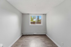 Room featuring a window with white trim, wood-finish flooring, light gray walls, white baseboards, and a baseboard heater - 