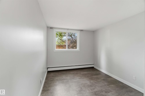Windowed room featuring light gray walls, dark wood-finish flooring, and white baseboards - 121 5125 Riverbend Road Nw, Edmonton, AB 
