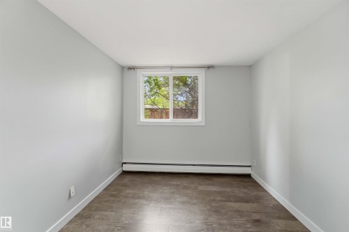 Room featuring light gray walls, wood-finish flooring, and a white-framed window - 121 5125 Riverbend Road Nw, Edmonton, AB 