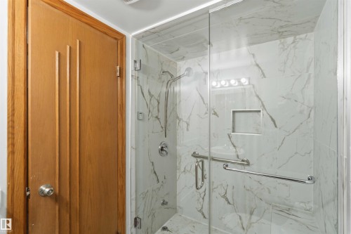 Glass-enclosed shower with white and grey marbled tile, recessed shower niche, and a chrome shower head and fixtures - 121 5125 Riverbend Road Nw, Edmonton, AB 