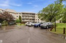 Multi-story building featuring private balconies, a prominent entrance, and an expansive paved parking area - 121 5125 Riverbend Road Nw, Edmonton, AB 