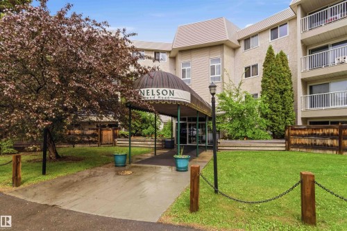 Entrance featuring a covered awning, established landscaping, and a paved walkway leading to the building - 121 5125 Riverbend Road Nw, Edmonton, AB 