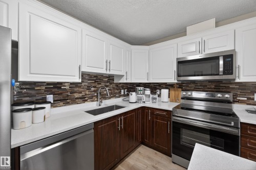 Kitchen featuring white upper cabinetry, rich wood-finish lower cabinetry, and a mosaic tile backsplash - 138 16035 132 Street, Edmonton, AB 