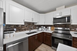 Kitchen featuring white upper cabinetry, rich wood-finish lower cabinetry, and a mosaic tile backsplash - 