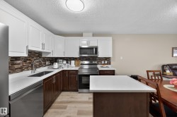 Open-concept kitchen featuring white upper cabinetry, dark wood-finish lower cabinetry, and stainless steel appliances - 