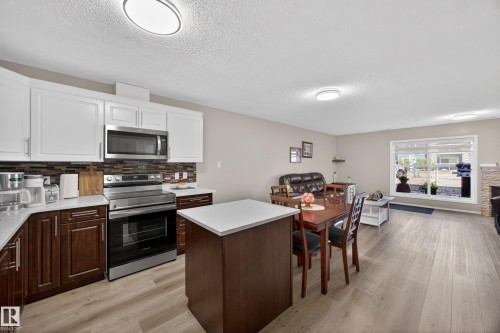 Open concept kitchen and dining area featuring two-tone cabinetry, stainless steel appliances, a tiled backsplash, and wood-finish flooring - 138 16035 132 Street, Edmonton, AB 
